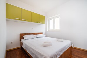 A bedroom with a wooden bed, white bedding, a green cabinet above, and a window on the right.