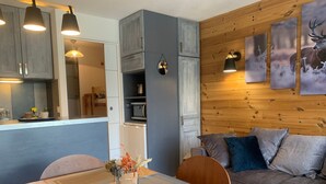 A cozy living area with a wooden wall, a sofa, and a dining table with placemats. - Renovated studio in Pra Loup with balcony and wifi, close to cable car (Pra-Loup)
