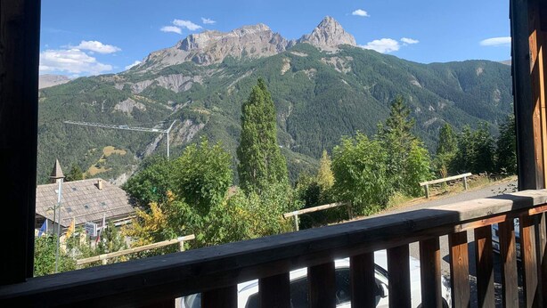 A mountain view from a balcony with a wooden railing, overlooking a valley with trees and a distant mountain peak. - Renovated studio in Pra Loup with balcony and wifi, close to cable car (Pra-Loup)