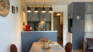 A modern kitchen with grey cabinets, a red coffee machine, and a dining area with a wooden table and chairs. - Renovated studio in Pra Loup with balcony and wifi, close to cable car (Pra-Loup)