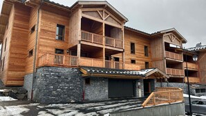 A multi-story wooden building with balconies, stone foundation, and a garage entrance. - Cosy Duplex, 3 Bedrooms + Bunk Area, Near Slopes, Garage, Ski Locker, No Smoking (Les Gets)