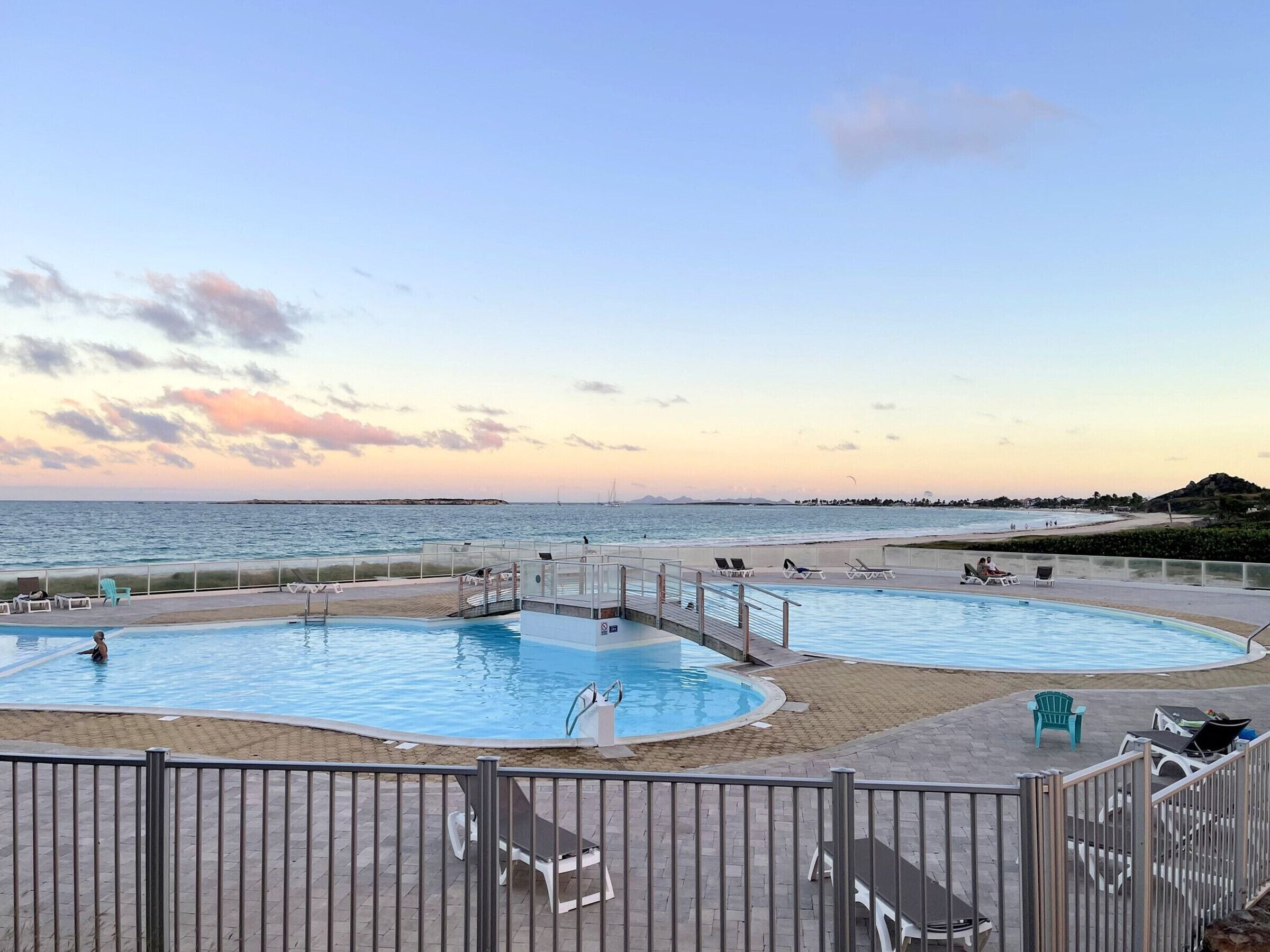 A pool area with two pools, lounge chairs, and a view of the beach and ocean.
