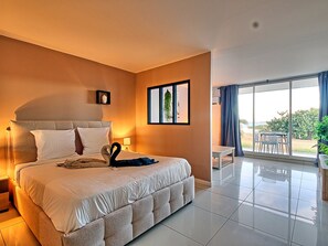 A hotel room with a large bed, a bedside table, a small table, and a view of the outdoors through a sliding glass door.