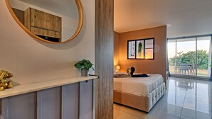 A modern bedroom with a large bed, a bedside table with a plant, a mirror, and a view of the outdoors through a large window. - Romantic Getaway Near Orient Bay Beach (Saint-Martin)