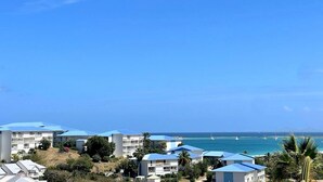 A coastal resort with multiple buildings featuring blue roofs, situated near a clear blue sea with boats visible in the distance. - Romantic Getaway Near Orient Bay Beach (Saint-Martin)