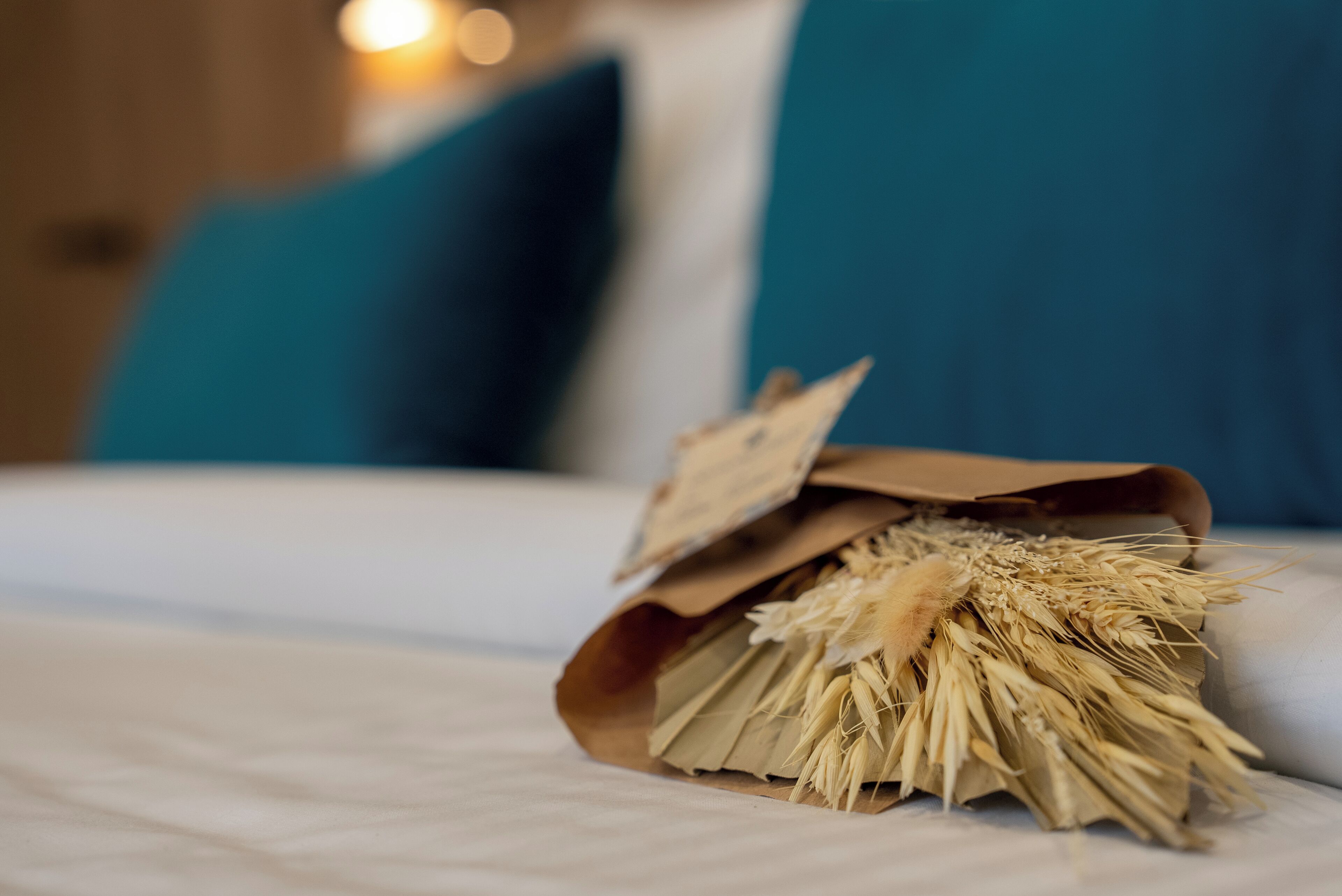 A bed with a brown paper bag containing dried wheat stalks on a white bedspread.