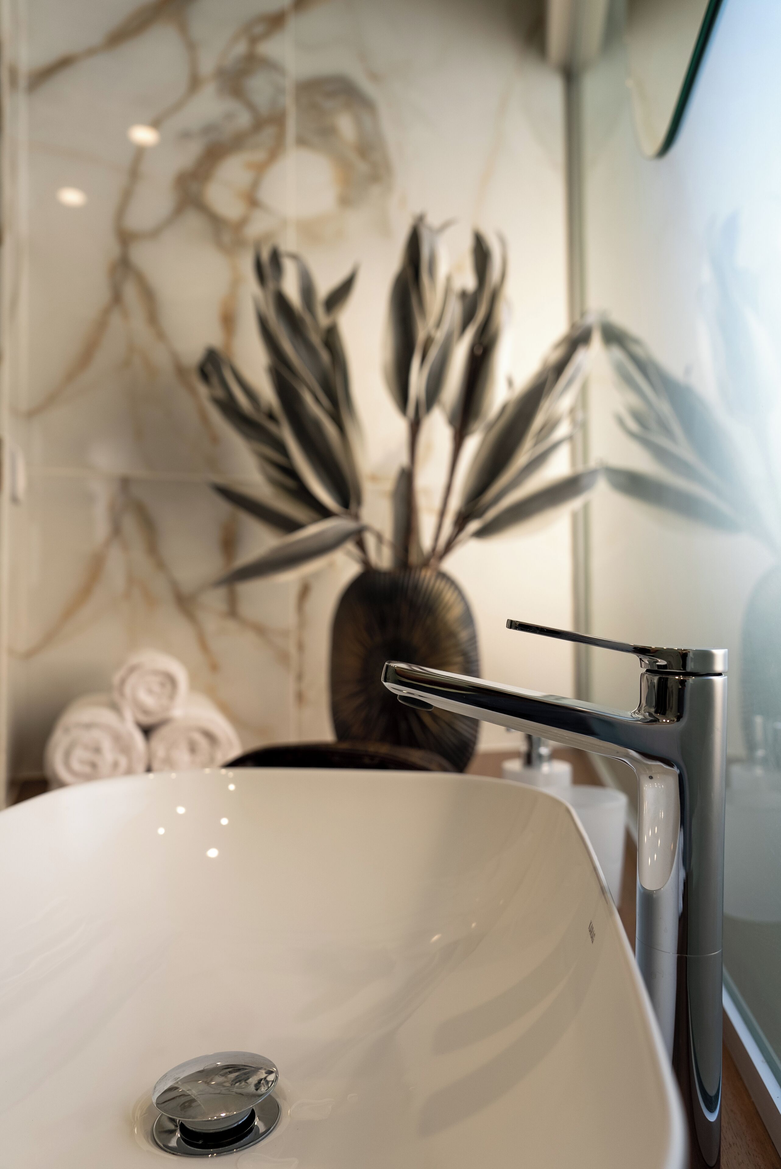 Un baño con un lavamanos blanco, un grifo moderno y una planta decorativa al fondo.
