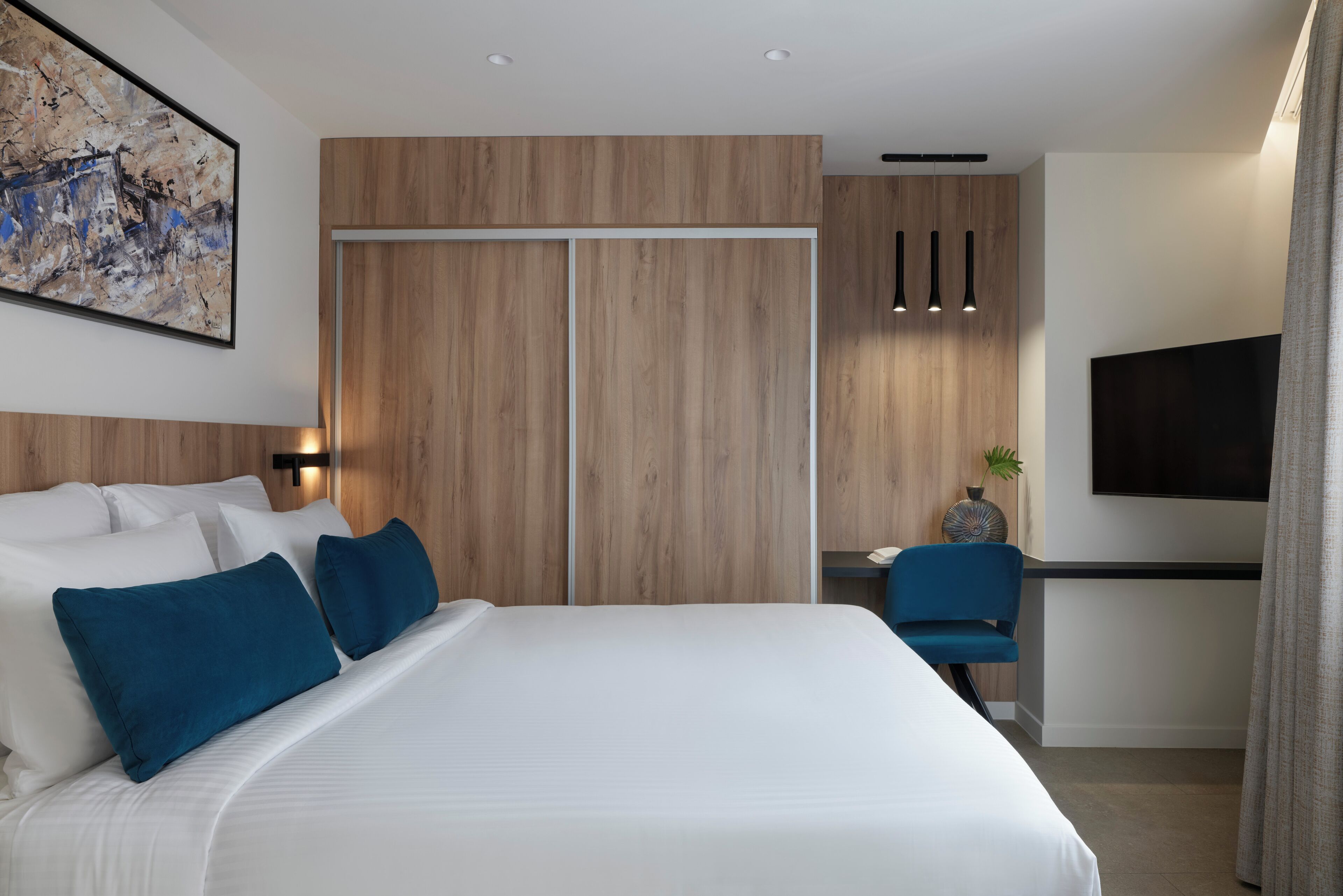 A modern hotel room with a large bed, a desk, and a TV.