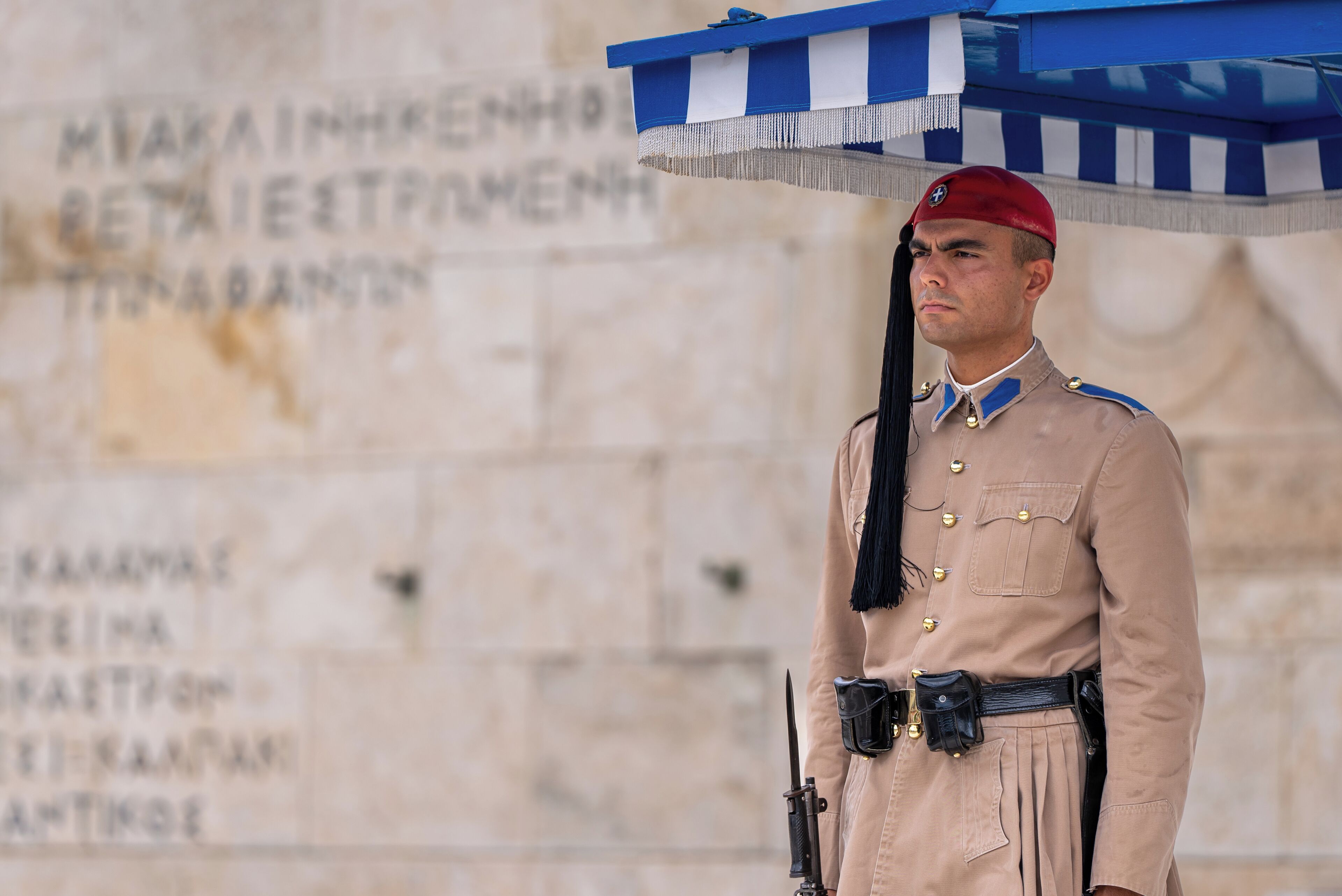 A uniformed guard standing in front of a stone wall with inscriptions.