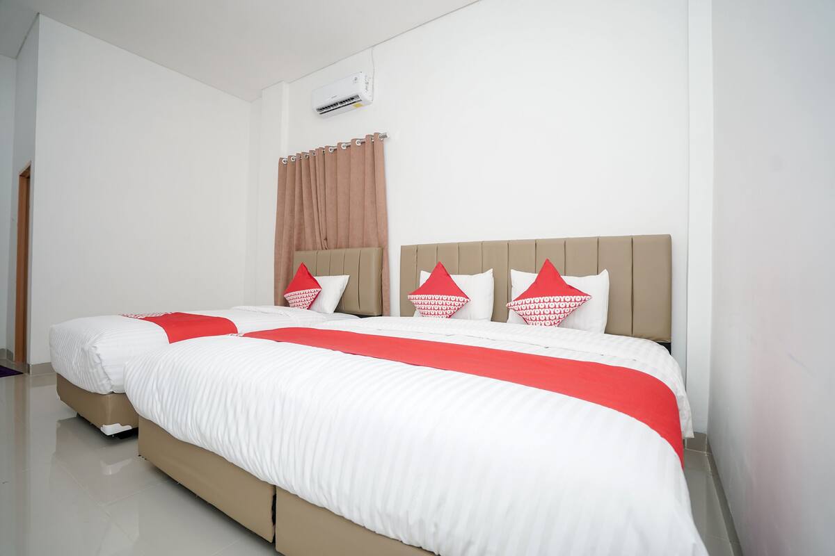 Una cama bien hecha con ropa de cama blanca y detalles rojos, un cabecero color beige y una cortina marrón.