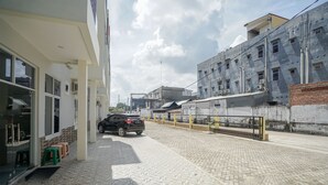 En asfalterad gata med en svart SUV parkerad vid sidan, byggnader med synliga fönster och luftkonditioneringsaggregat, och en klar himmel.