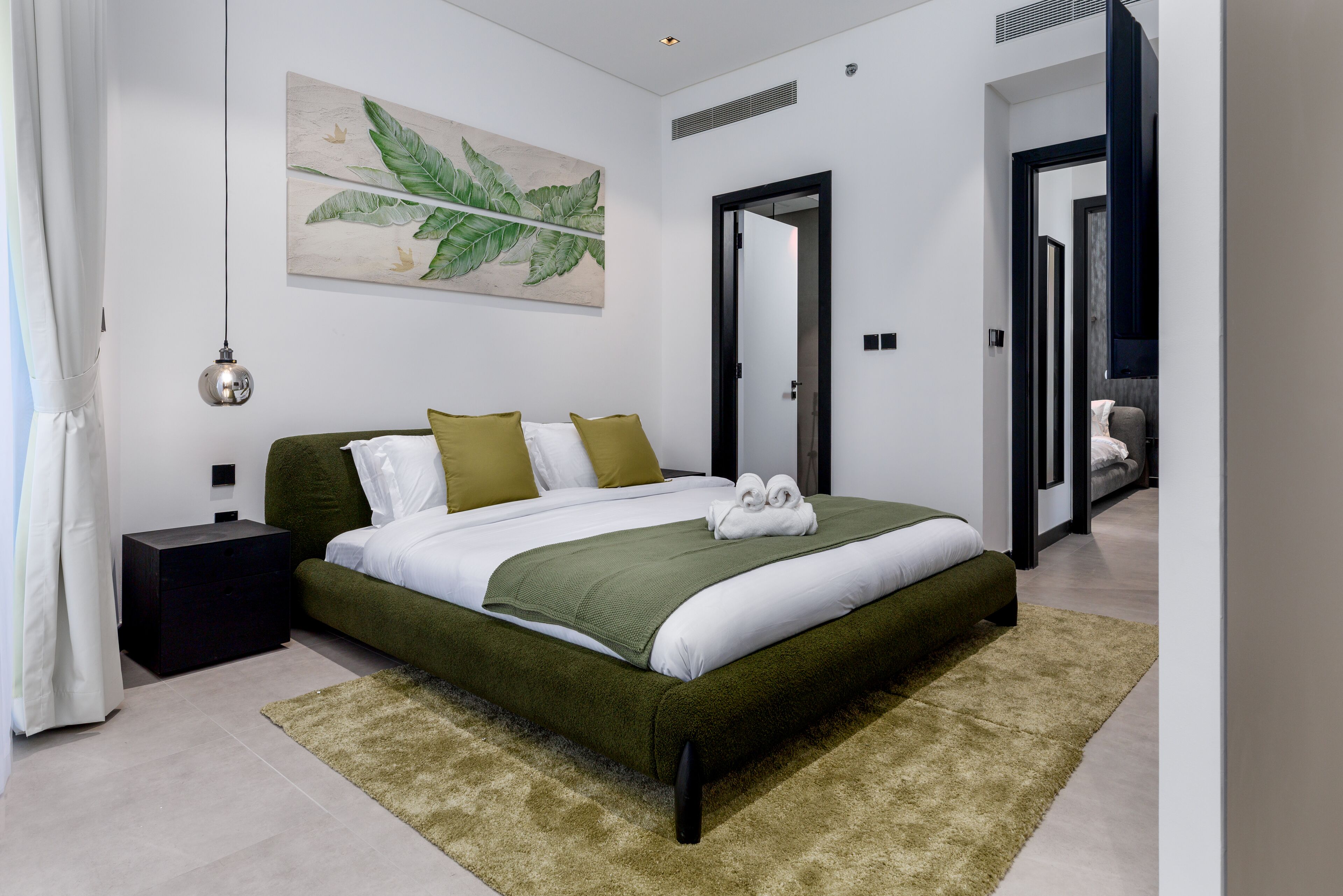 Une chambre moderne avec un grand lit, une table de chevet, un plaid vert et une œuvre d’art accrochée au mur.