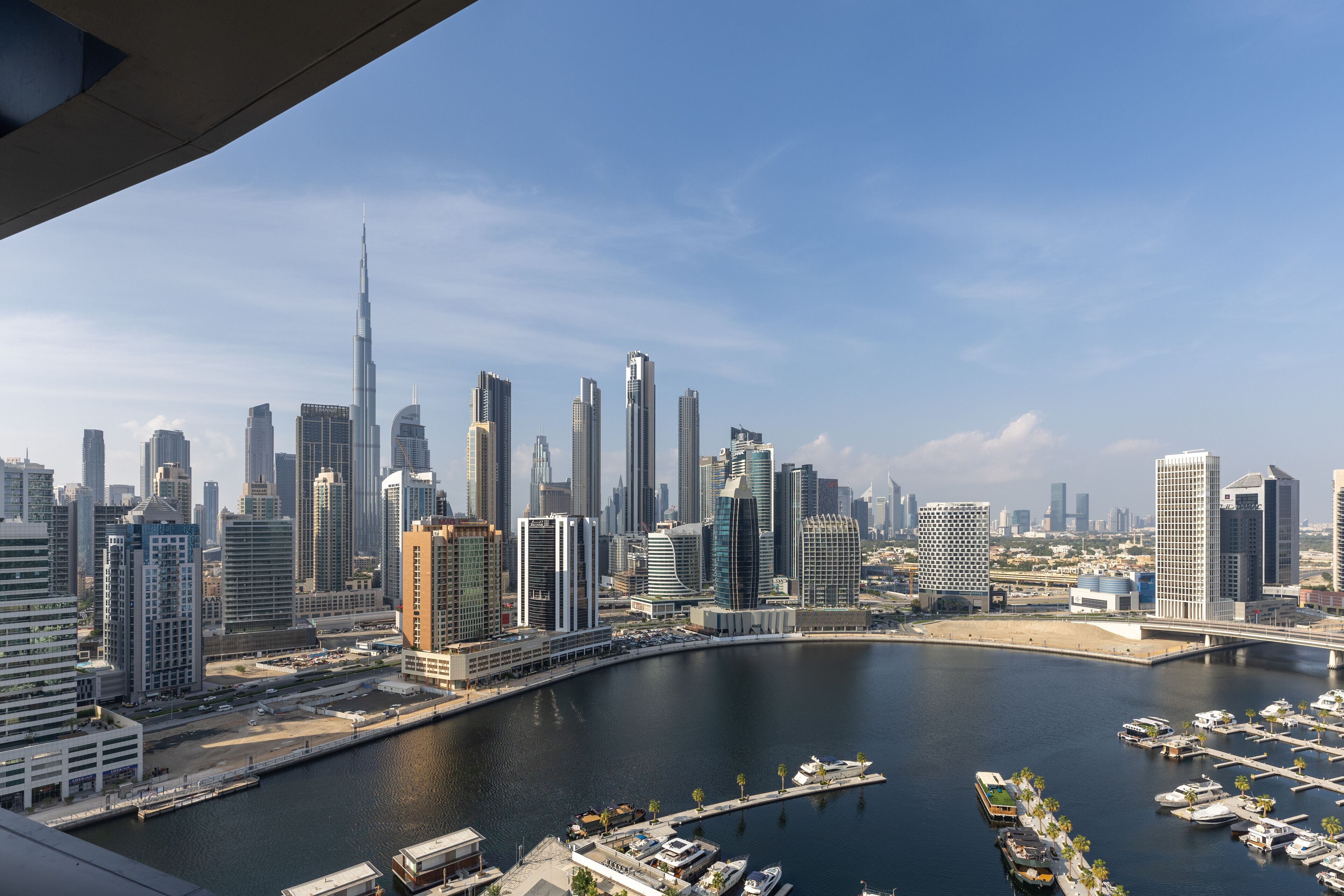 A cityscape with modern skyscrapers, a marina with boats, and a clear sky.