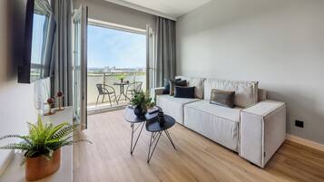 Una sala de estar moderna con un sofá gris, una mesita con una planta y vistas a la ciudad a través de amplias ventanas.