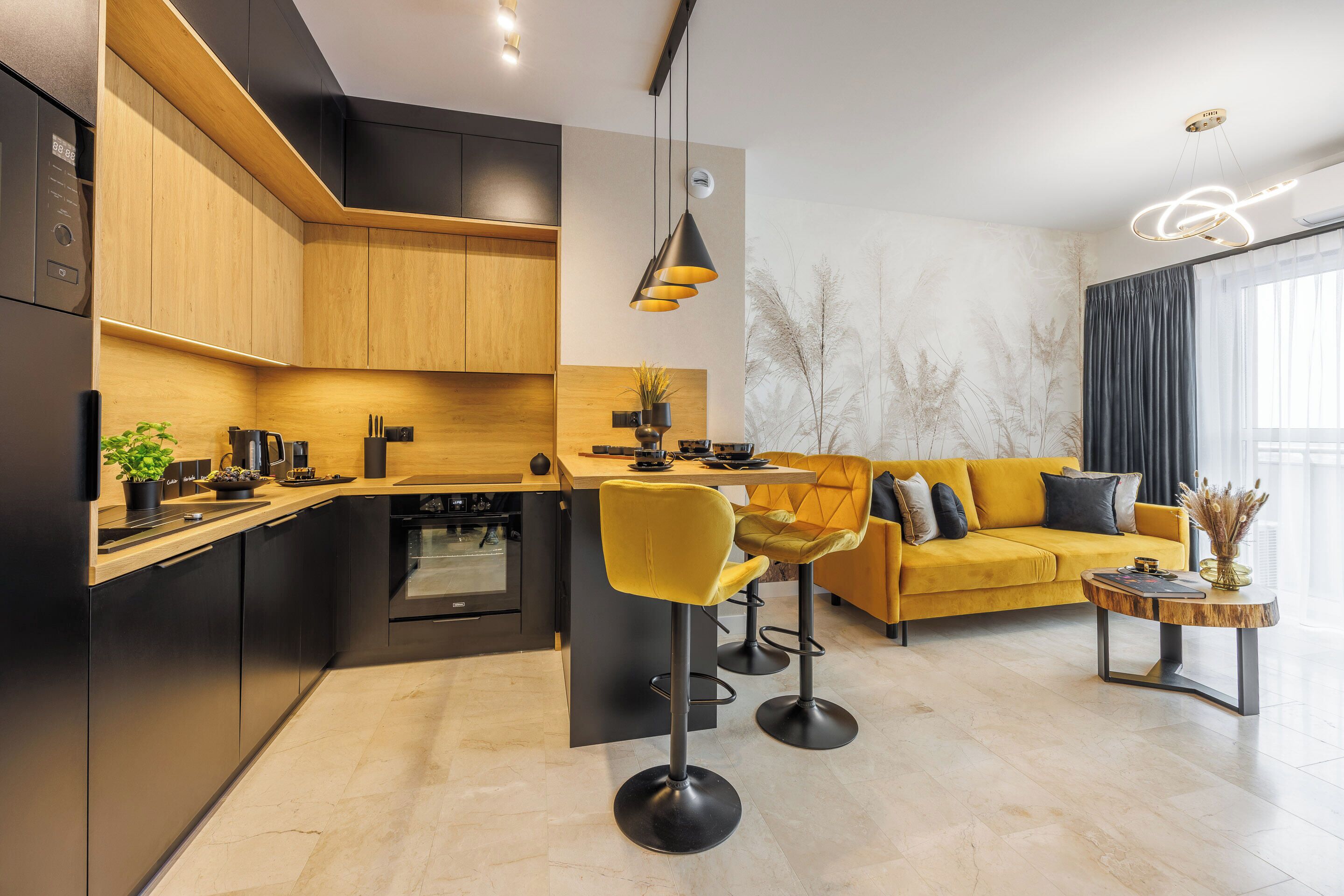 Uma cozinha moderna com ilha central, banquetas de bar e um sofá amarelo em uma sala de estar com uma janela grande.