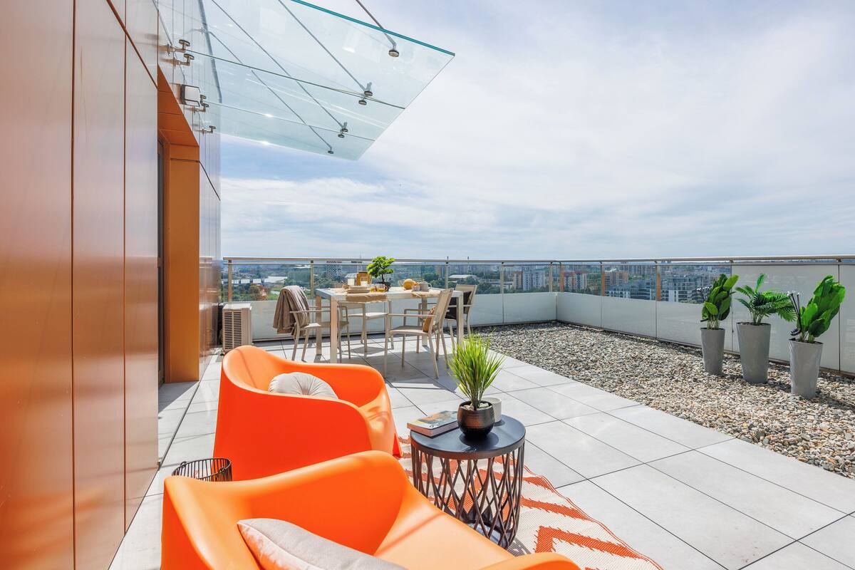 A rooftop terrace with orange seating, a table, and potted plants.