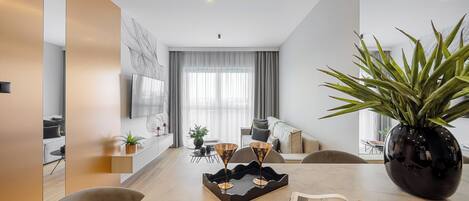 Una sala de estar moderna con comedor, que incluye una planta grande en maceta, una revista sobre la mesa y un televisor montado en la pared.