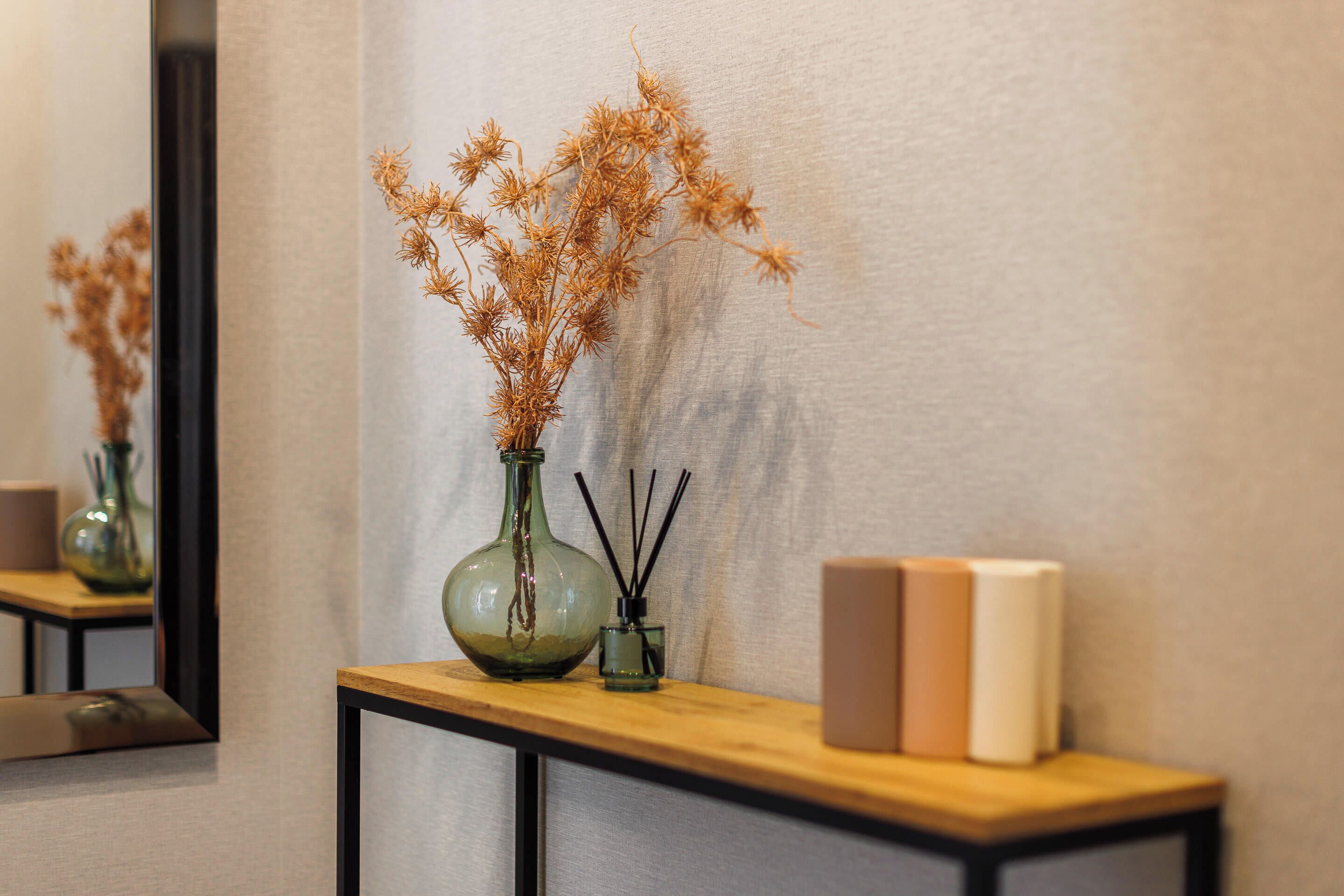 A wooden console table with a vase of dried flowers, a small glass container with reed sticks, and two books.