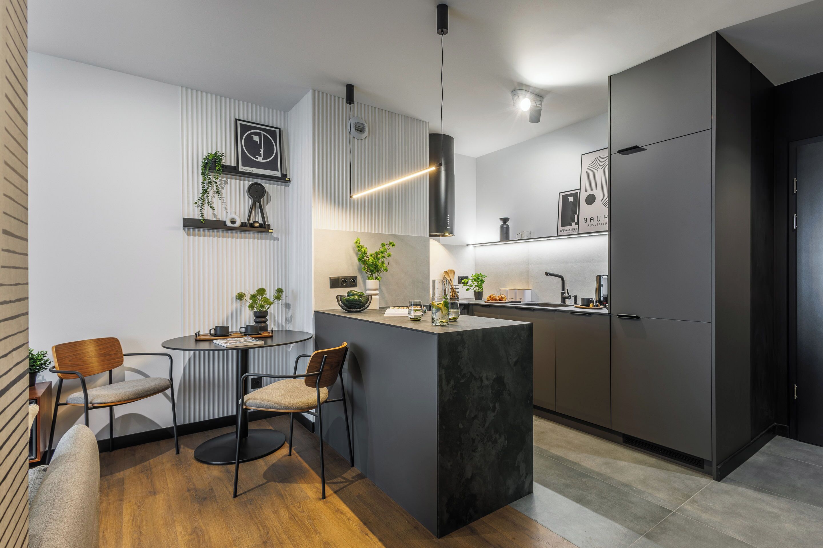 Une cuisine moderne dotée d’un îlot central, de meubles de couleur sombre et d’un luminaire suspendu.