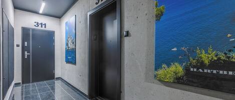 Un pasillo con dos puertas identificadas con el número 311, un ascensor y un cartel grande con una escena costera.
