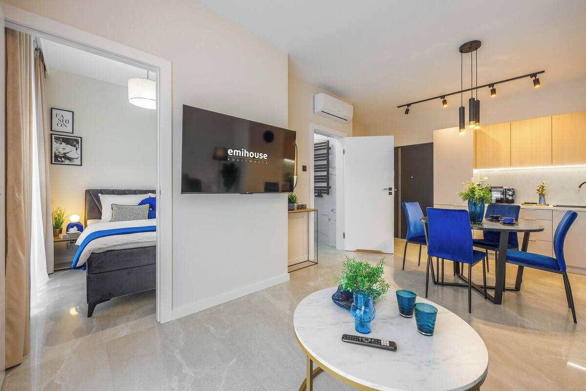 A modern hotel room with a bed, a TV, a dining area with chairs and a table, and a small balcony.