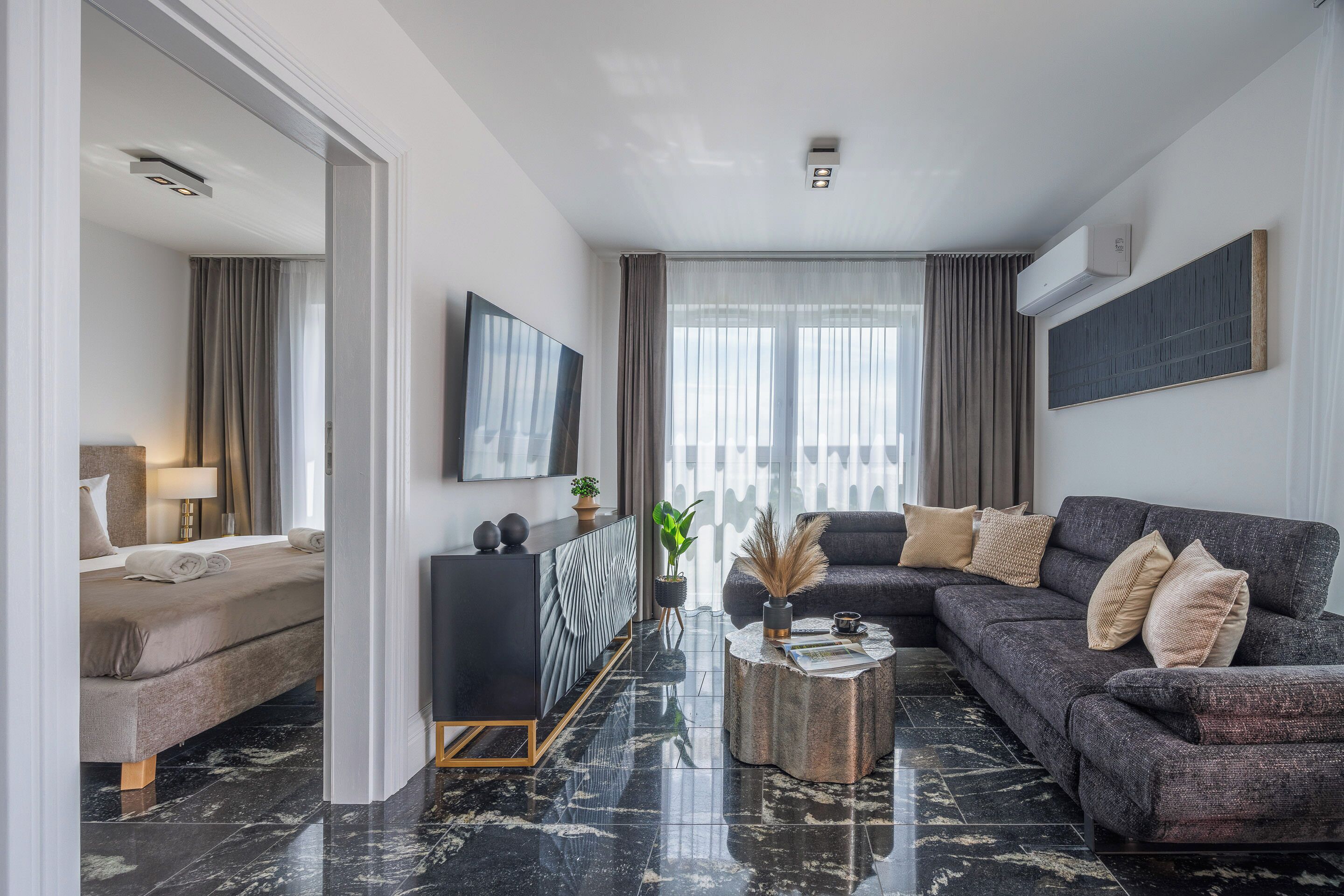 A modern living room with a sofa, coffee table, and a bed in the adjacent room.