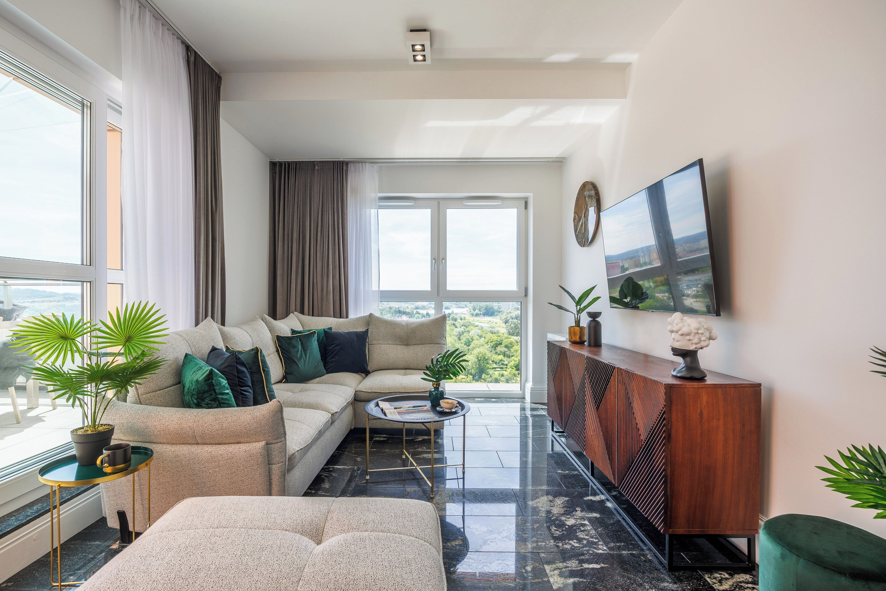 A modern living room with a sectional sofa, a coffee table, and a large flat-screen TV mounted on the wall.