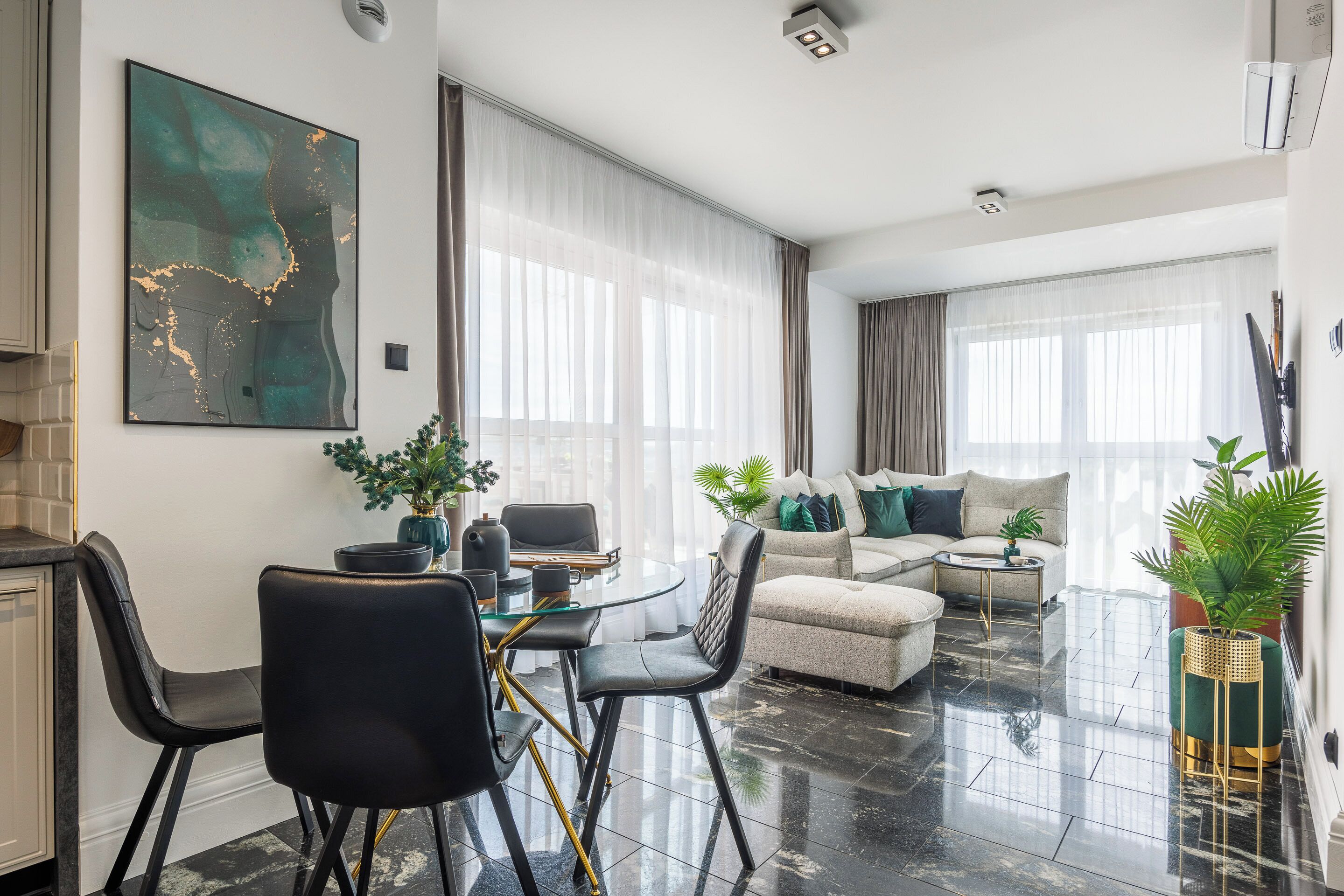 A modern living room with a glass dining table, black chairs, a beige sofa, and a green accent chair.