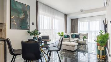 A modern living room with a glass dining table, black chairs, a beige sofa, and a green accent chair.