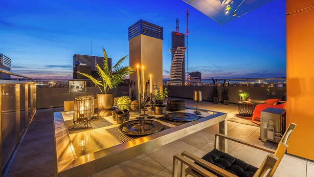 Una terraza en la azotea con un área de bar moderna, asientos y vistas del horizonte de la ciudad al anochecer.