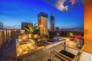 A rooftop terrace with a modern bar area, seating, and a view of the city skyline at dusk. - Emihouse Riverside Apartments (Rzeszów)