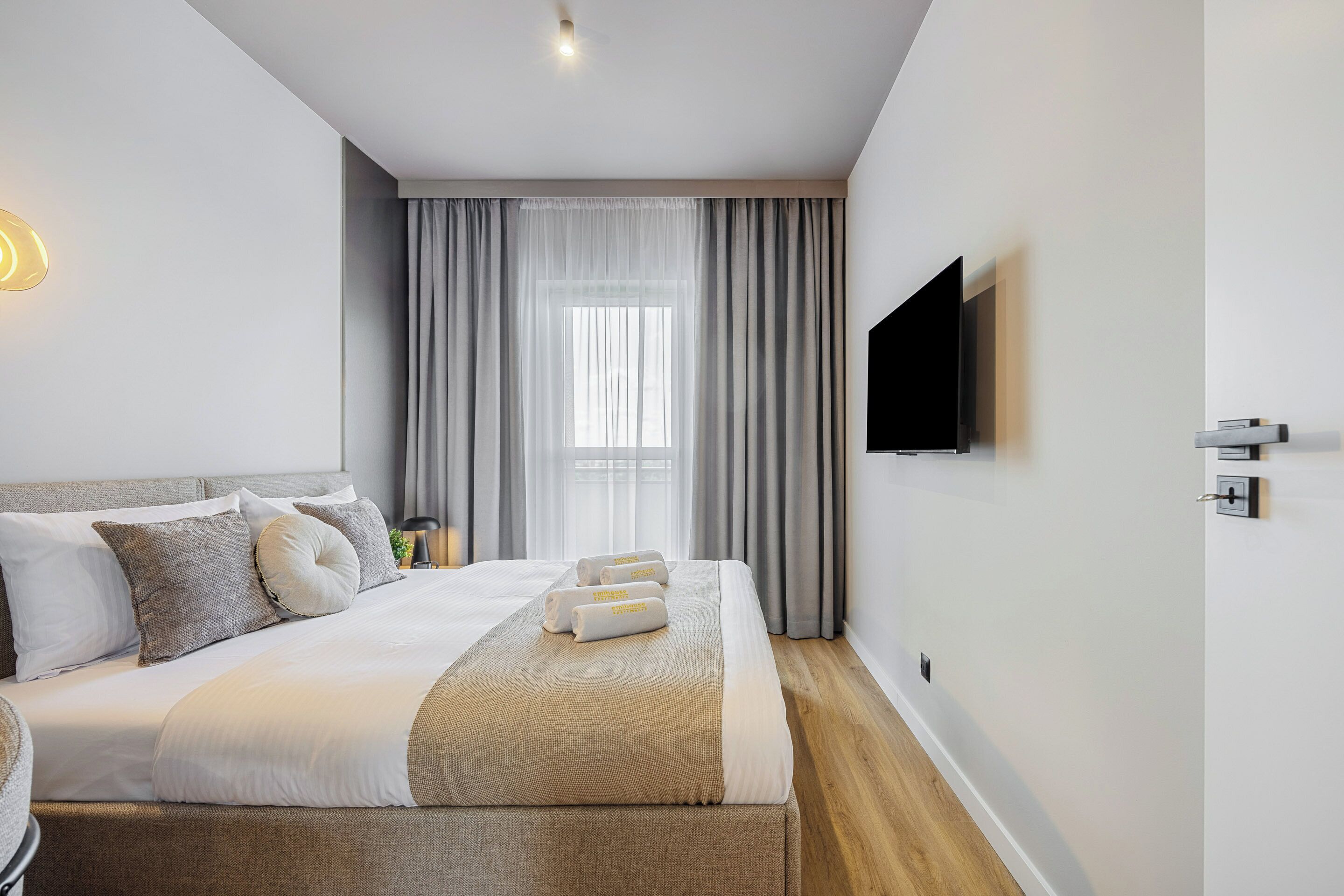 A modern hotel room with a large bed, a flat-screen TV, and a window with curtains.