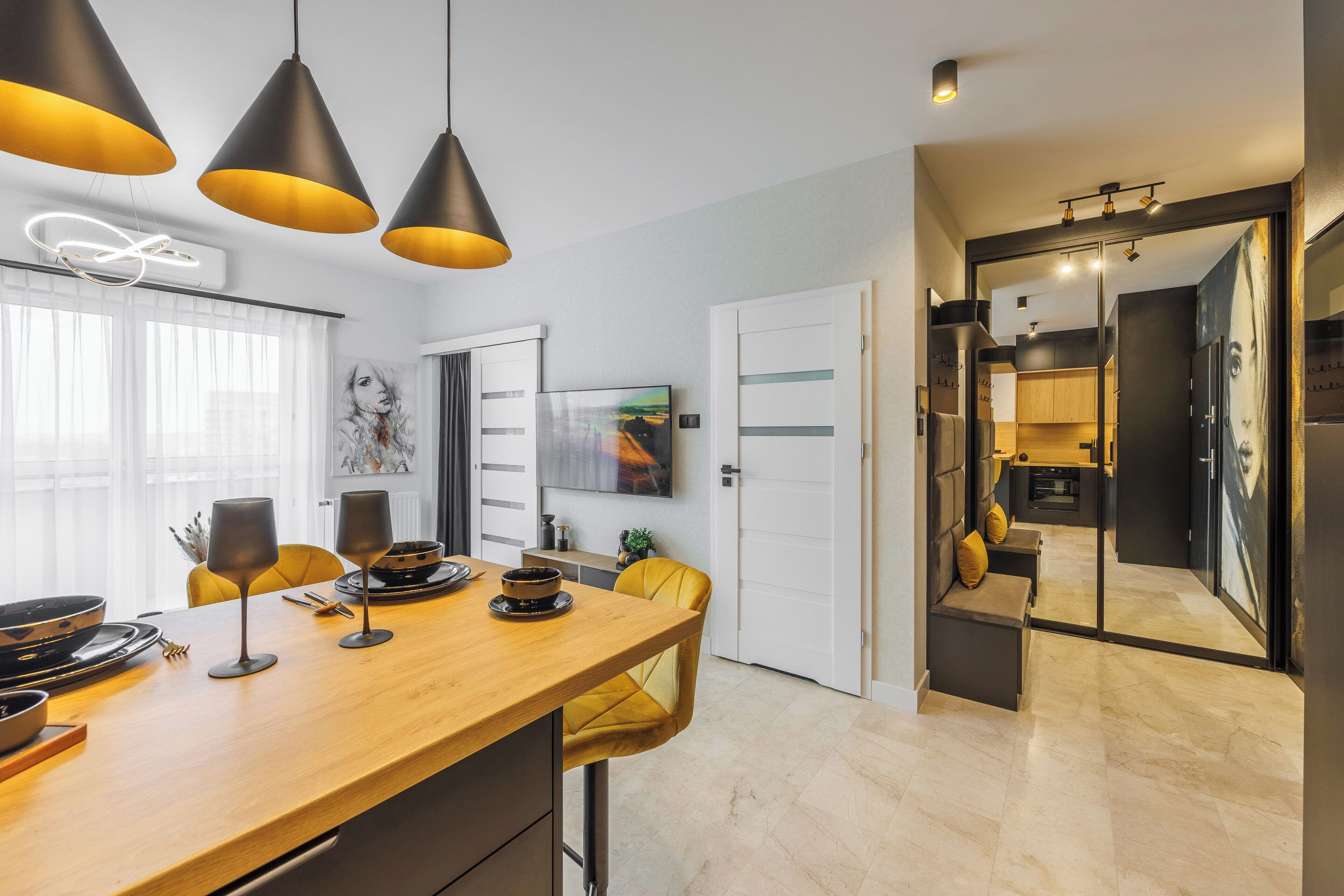 Una cucina moderna con piano di lavoro in legno, lampade a sospensione nere e un'area pranzo con sedie gialle.