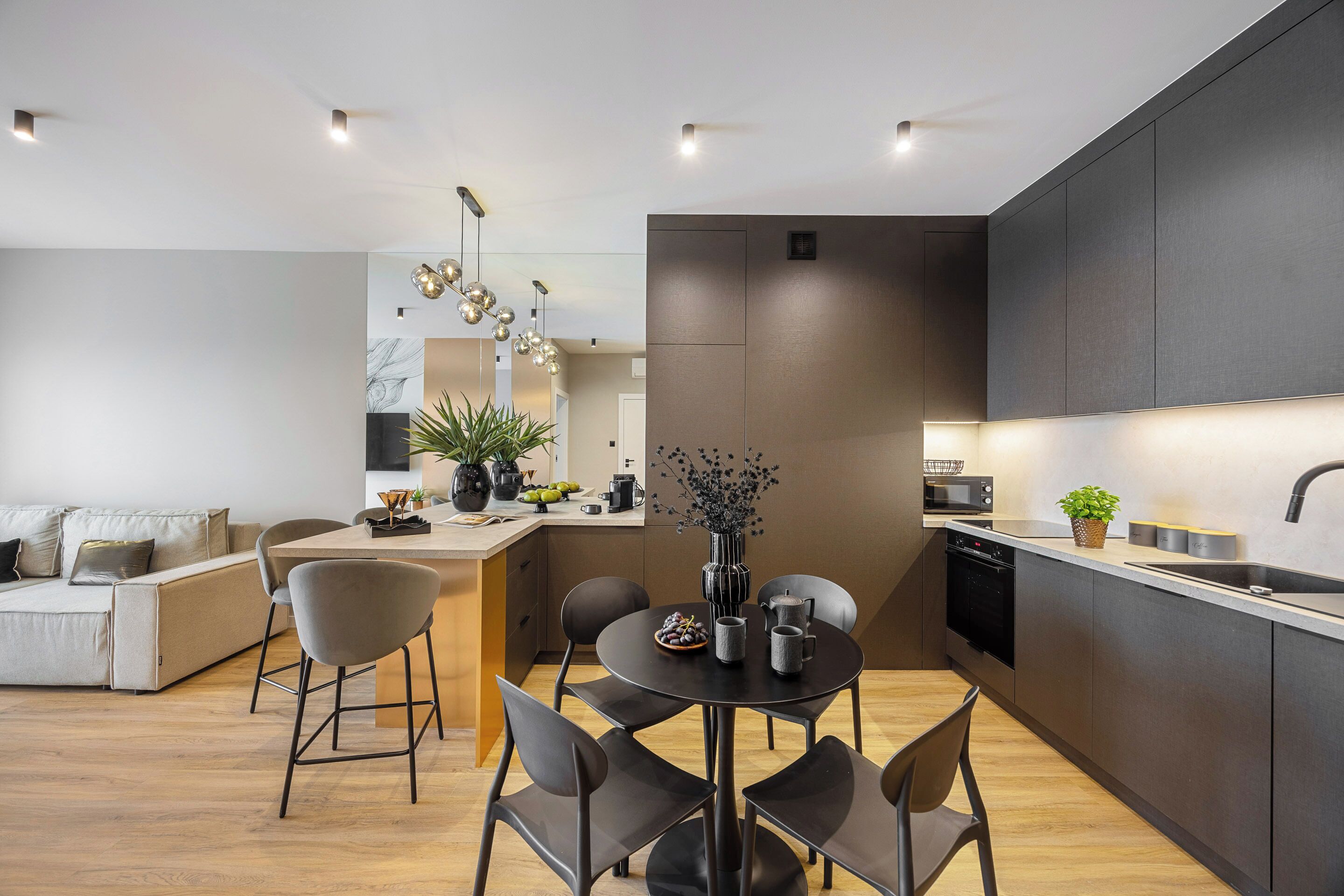 A modern kitchen with a dining area, featuring a central island, dark cabinetry, and contemporary lighting fixtures.