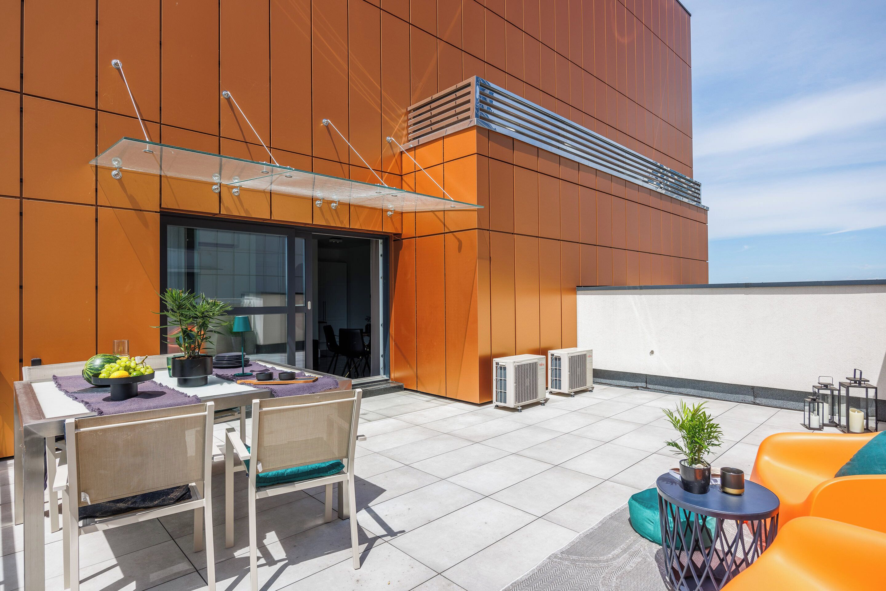 Un patio al aire libre con una mesa, sillas, equipos de aire acondicionado y asientos anaranjados.