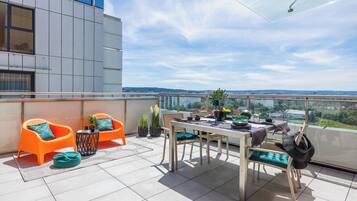 Una terraza moderna al aire libre con una mesa de comedor, dos sillas color naranja, una mesita negra y una planta en maceta.