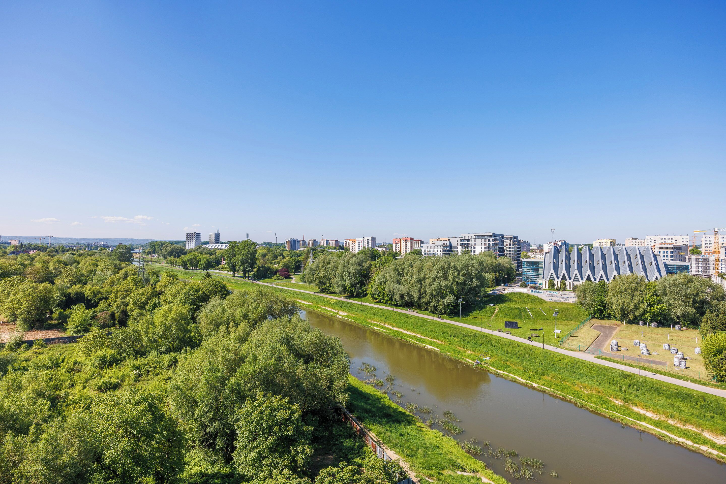 Une rivière traverse un parc, avec des arbres et des bâtiments en arrière-plan.