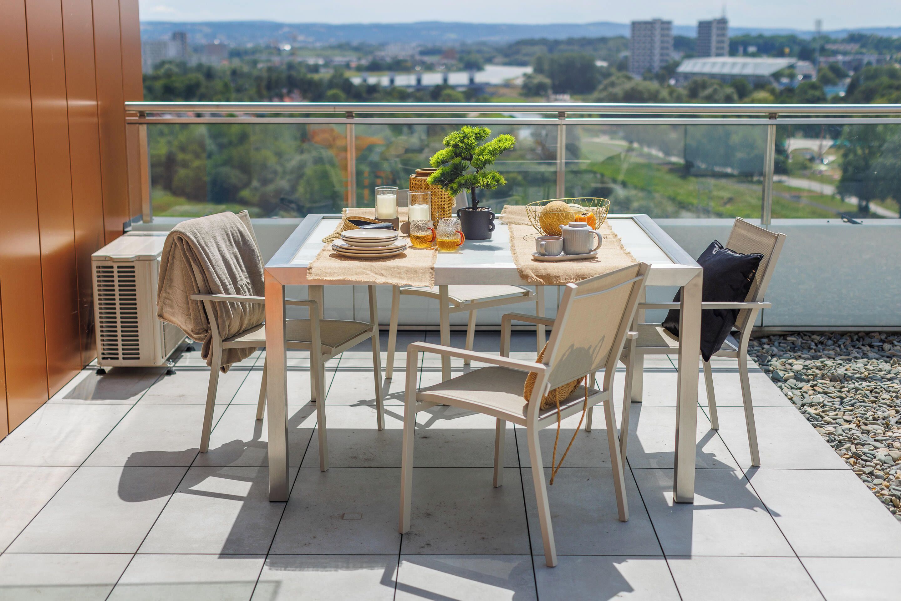 Een balkon met een eettafel, een bloempot en uitzicht op de stad.