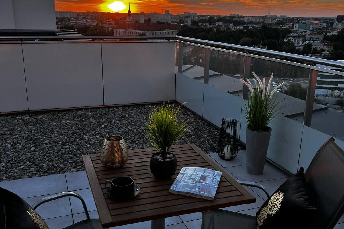 A rooftop terrace with a table, chairs, potted plants, and a sunset view.