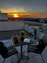 Terraza en la azotea con mesa, sillas, plantas en macetas y vistas del atardecer.