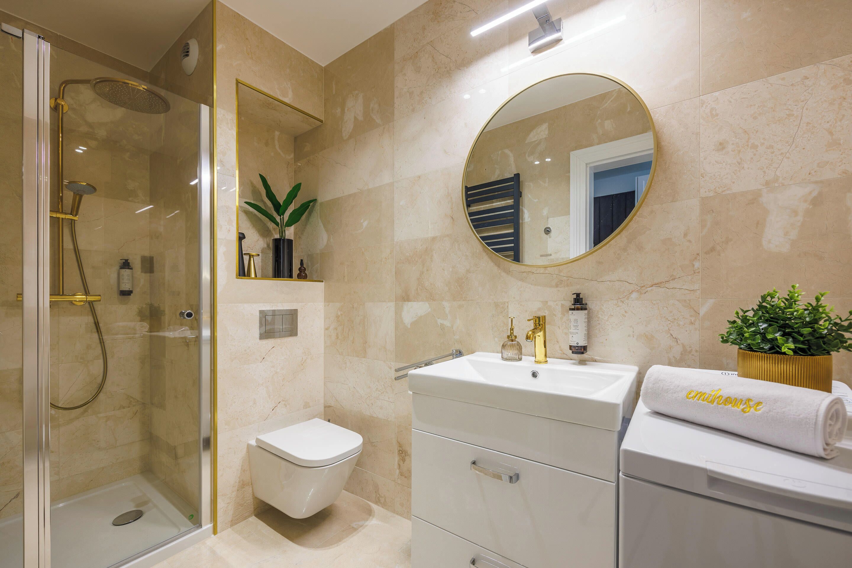 Een moderne badkamer met een douche met glazen wand, een toilet, een wastafel met spiegel en een handdoek met de tekst 'enjoyse'.