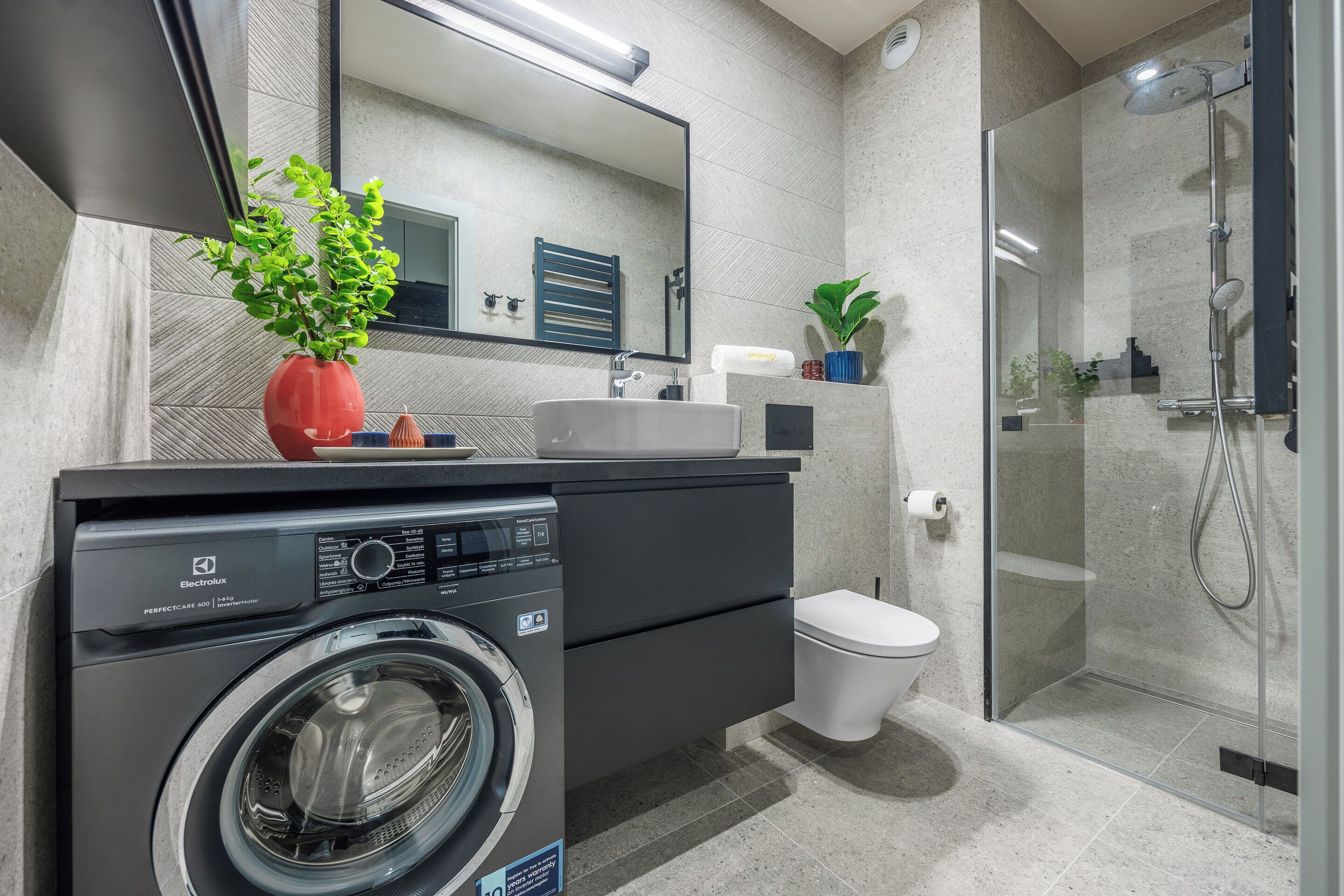 A modern bathroom with a washing machine, a toilet, a glass-enclosed shower, and a large mirror.
