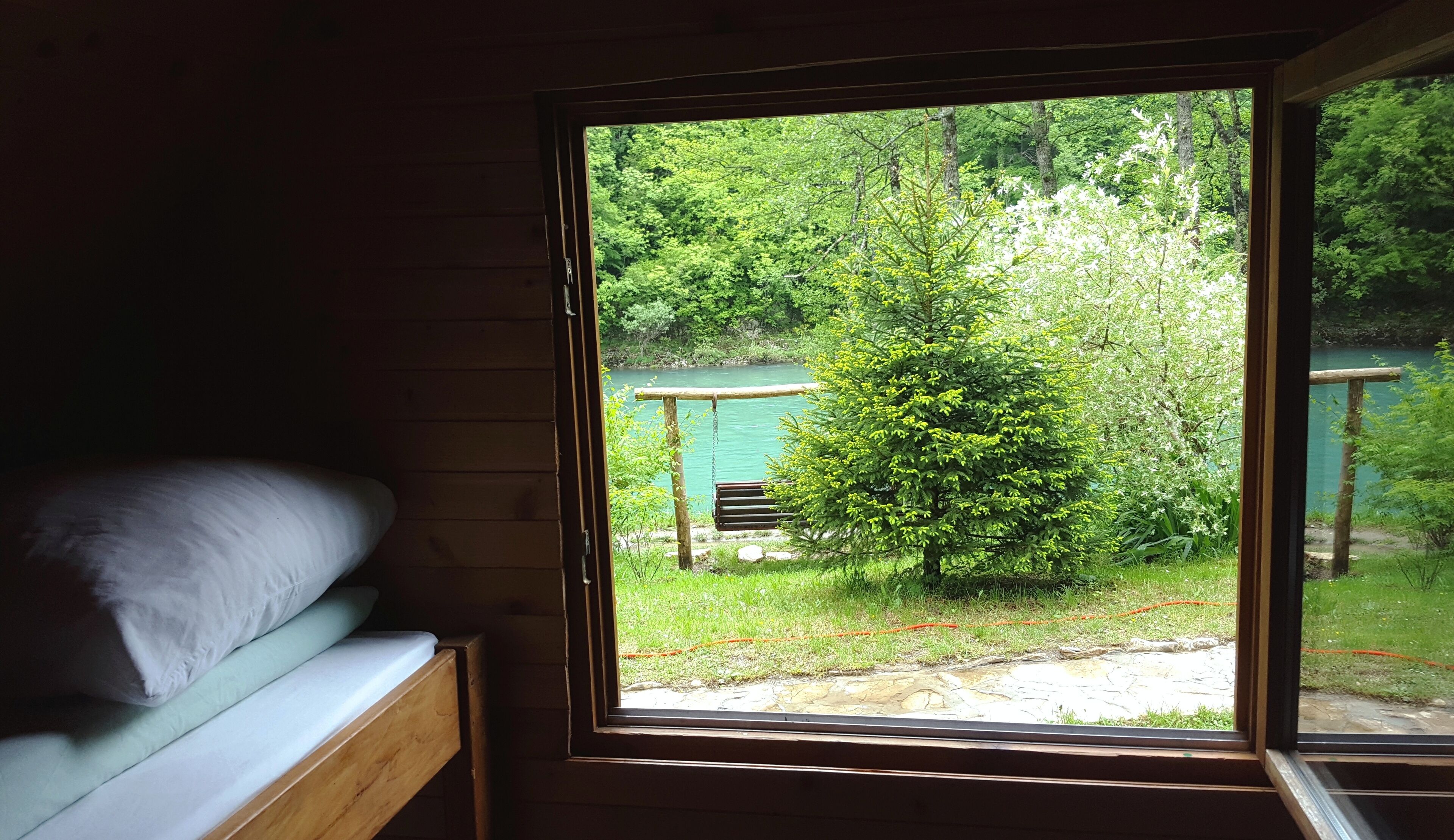 A cabin with a bed and a window overlooking a forest and a lake.