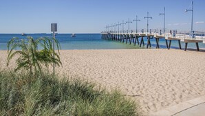 Une plage avec une jetée qui s’avance dans l’océan, agrémentée de lampadaires et d’un panneau indicateur.