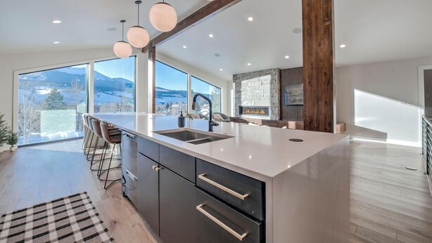 Une cuisine moderne dotée d’un grand îlot central, de tabourets de bar, d’une cheminée et offrant une vue sur les montagnes.