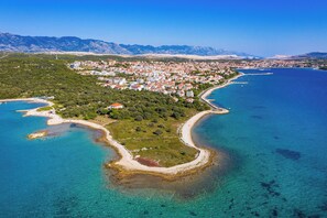 An aerial view of a coastal town with a beach, clear blue waters, and a mountainous backdrop. - Room-cozy Room Near Beach D (Novalja)