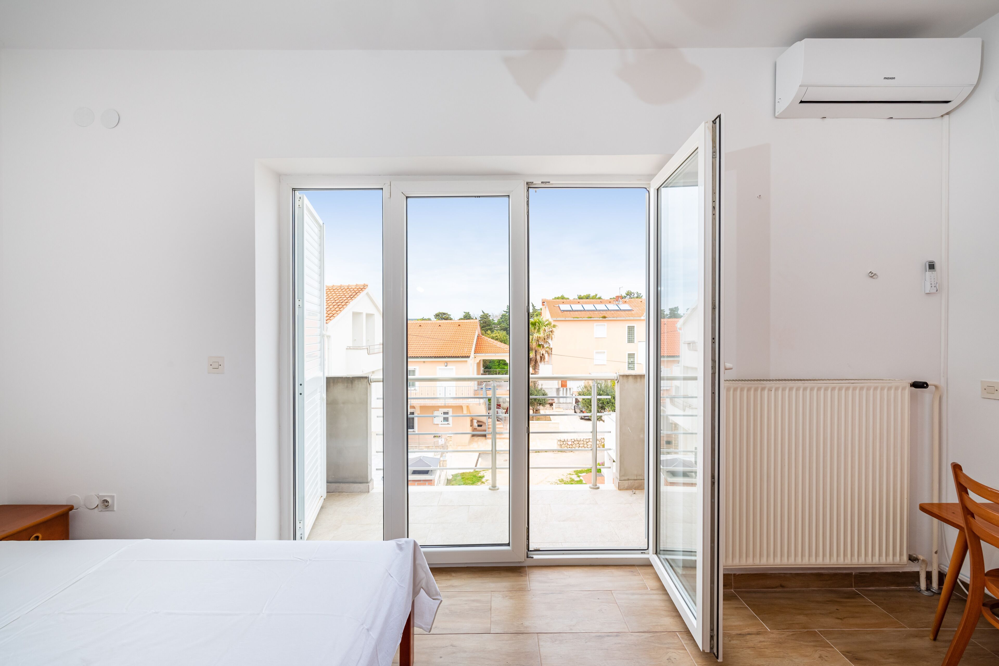 A room with a bed, a table, a chair, a radiator, and a sliding glass door leading to an outdoor area.