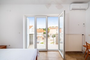 A room with a bed, a table, a chair, a radiator, and a sliding glass door leading to an outdoor area. - Room-cozy Room Near Beach D (Novalja)