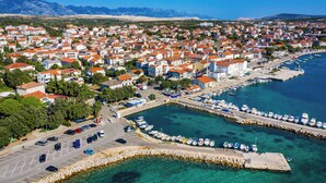 An aerial view of a coastal town with a marina, clear blue waters, and a mountainous backdrop. - Room-cozy Room Near Beach D (Novalja)