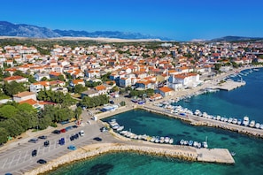 An aerial view of a coastal town with a marina, clear blue waters, and a mountainous backdrop. - Room-cozy Room Near Beach D (Novalja)